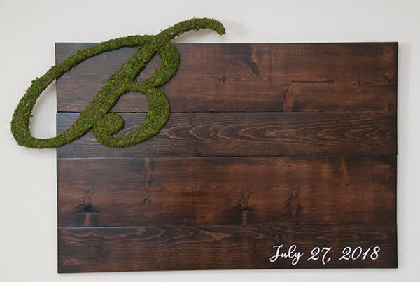 Personalized wedding sign-in board with moss-wrapped initial letter and rustic barn wood background for a cozy, intimate feel by Urban Garden Studio