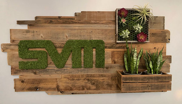 Elevate your space with a custom logo wrapped in preserved moss and integrated into a striking reclaimed wood living wall, featuring faux succulents, air plants, moss, and plants for a captivating visual display.