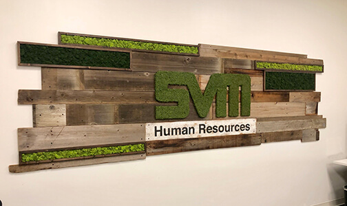 Custom moss logo wrapped in preserved moss and incorporated into a reclaimed wood living wall by Urban Garden Studio Create a stunning visual display with a custom moss logo created from preserved moss and incorporated into a reclaimed wood living wall, complete with preserved moss boxes featuring reindeer moss & hand painted logo by Urban Garden Studio