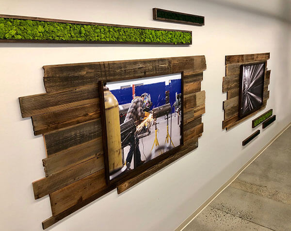 Custom office photos framed with rustic wood displayed on reclaimed wood wall adorned with preserved moss boxes, creating unique and sustainable office art display By Urban Garden Studio.